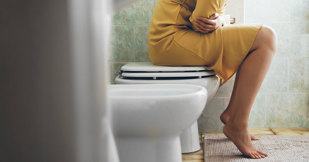 A woman seated on the toilet in discomfort.