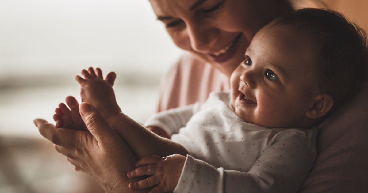 A mother holds her smiling baby in her arms.