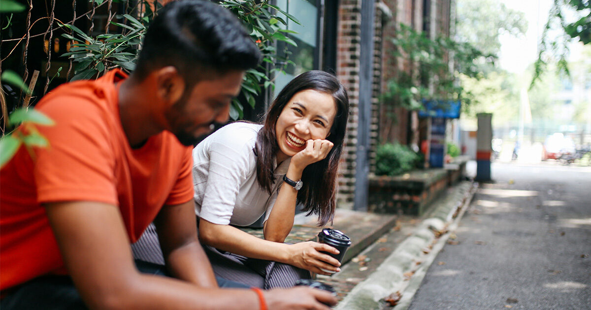 A young man and a young woman sit outdoors on a stoop engaged in conversation.