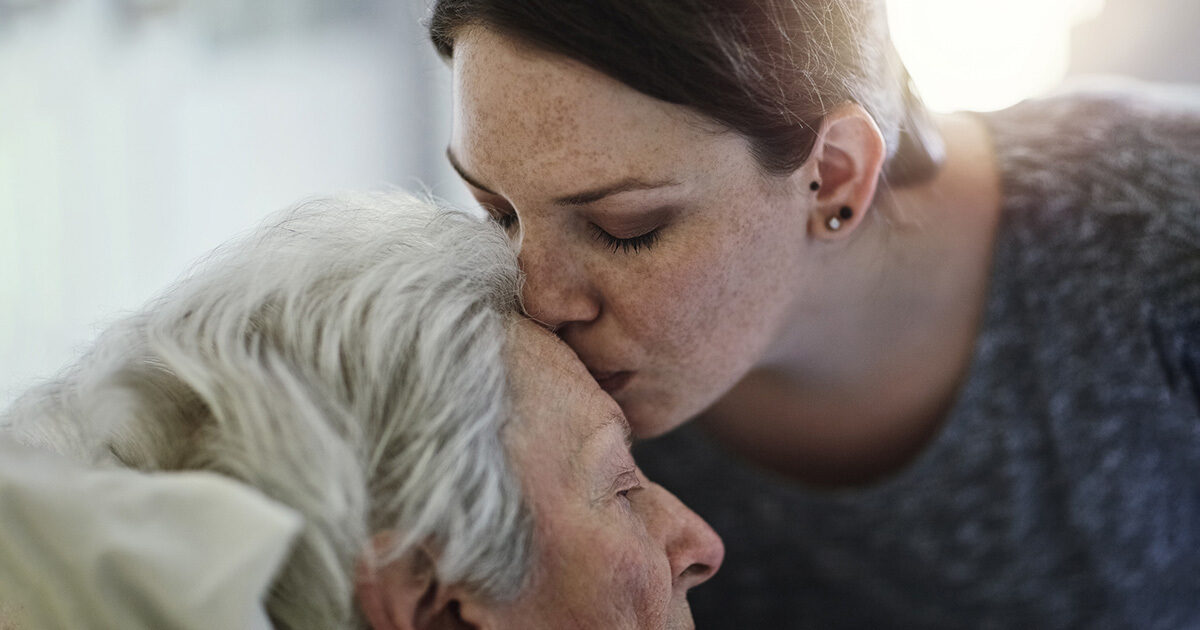 A woman kissing the forehead of her older loved one.