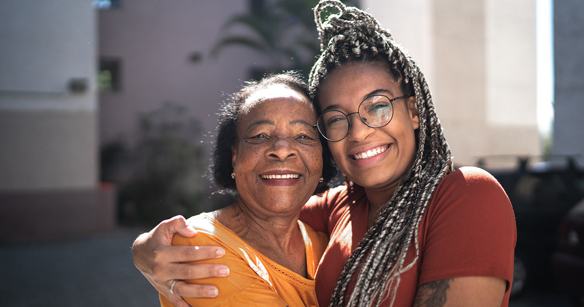 A Black mother and daughter hugging and smiling at camera.