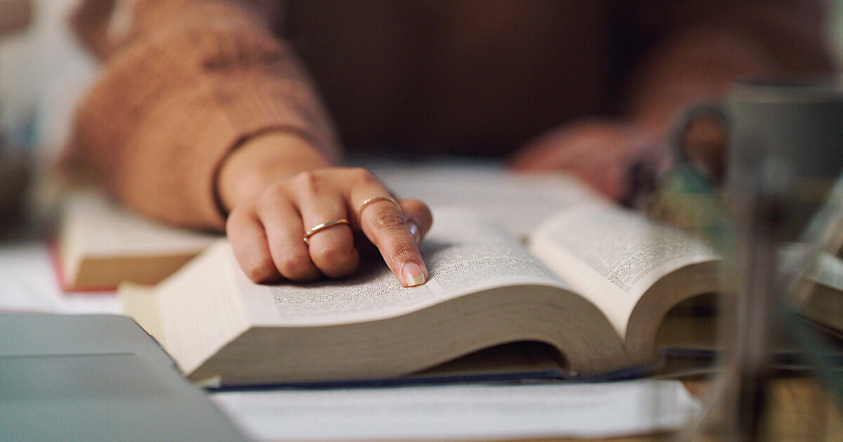 A hand with gold rings on two fingers pointing at text in a book.