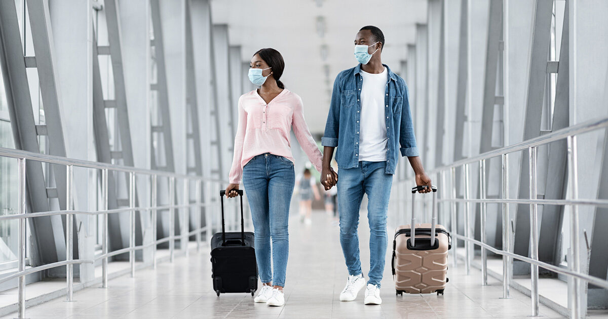 A couple wearing surgical masks tow their luggage through an airport.