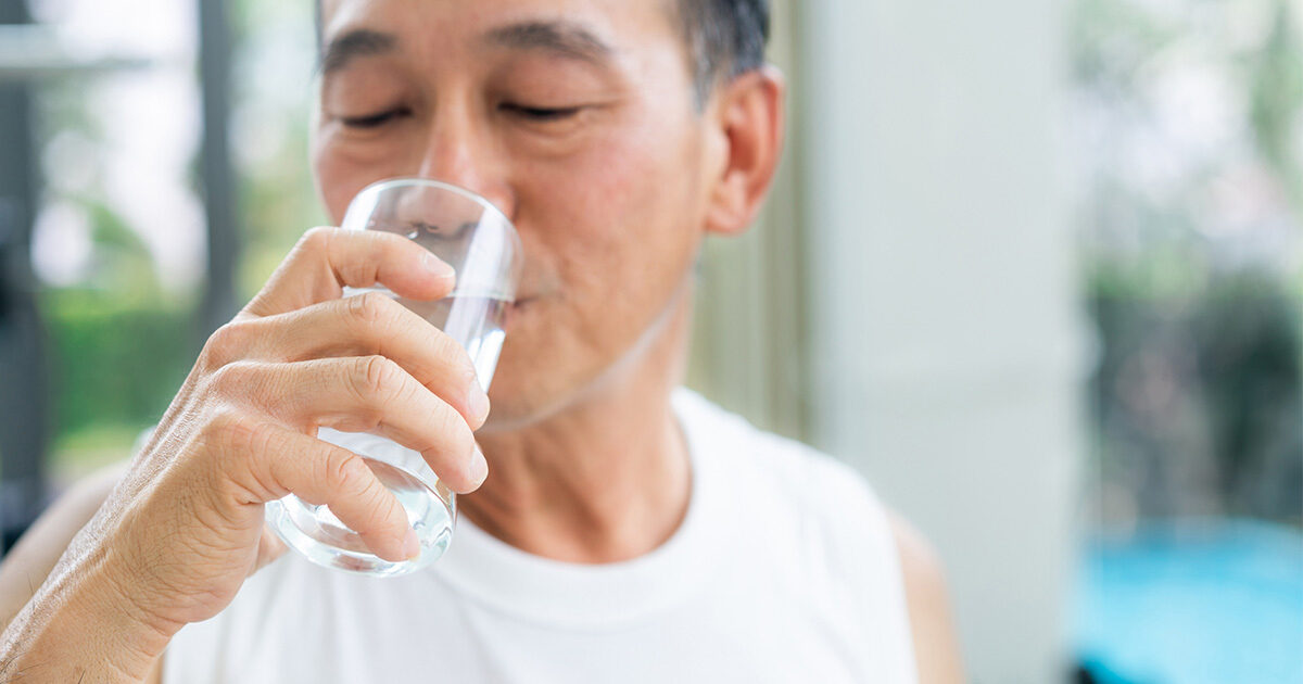 A middle-aged Asian man drinking a glass of water.