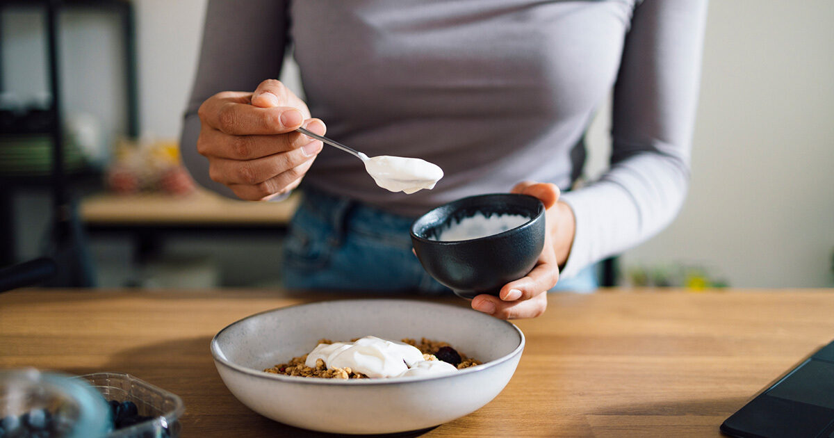 Close-up of a woman's hands as she scoops yogurt onto a bowl of granola.