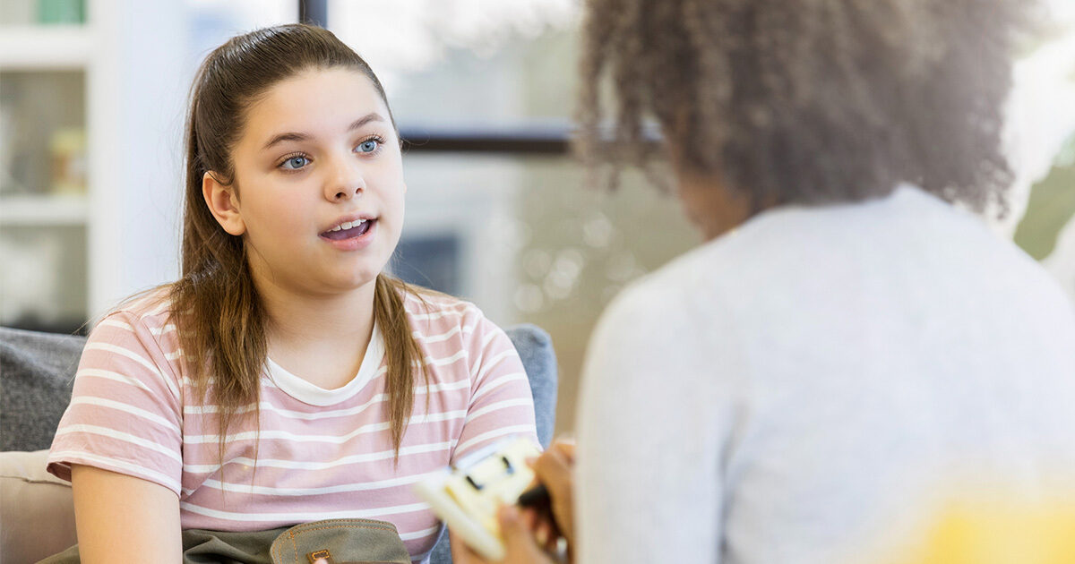 A young teenage girl speaking to a woman with a clipboard who is listening intently.