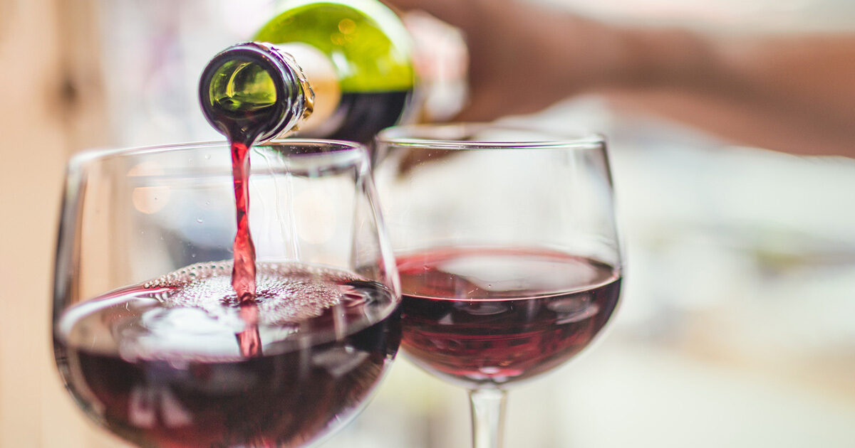 Close-up of wine being poured into one glass next to a glass that has already been filled.