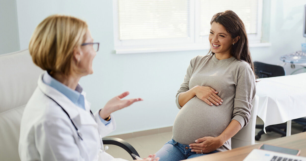 A pregnant woman speaking to a doctor at an appointment.