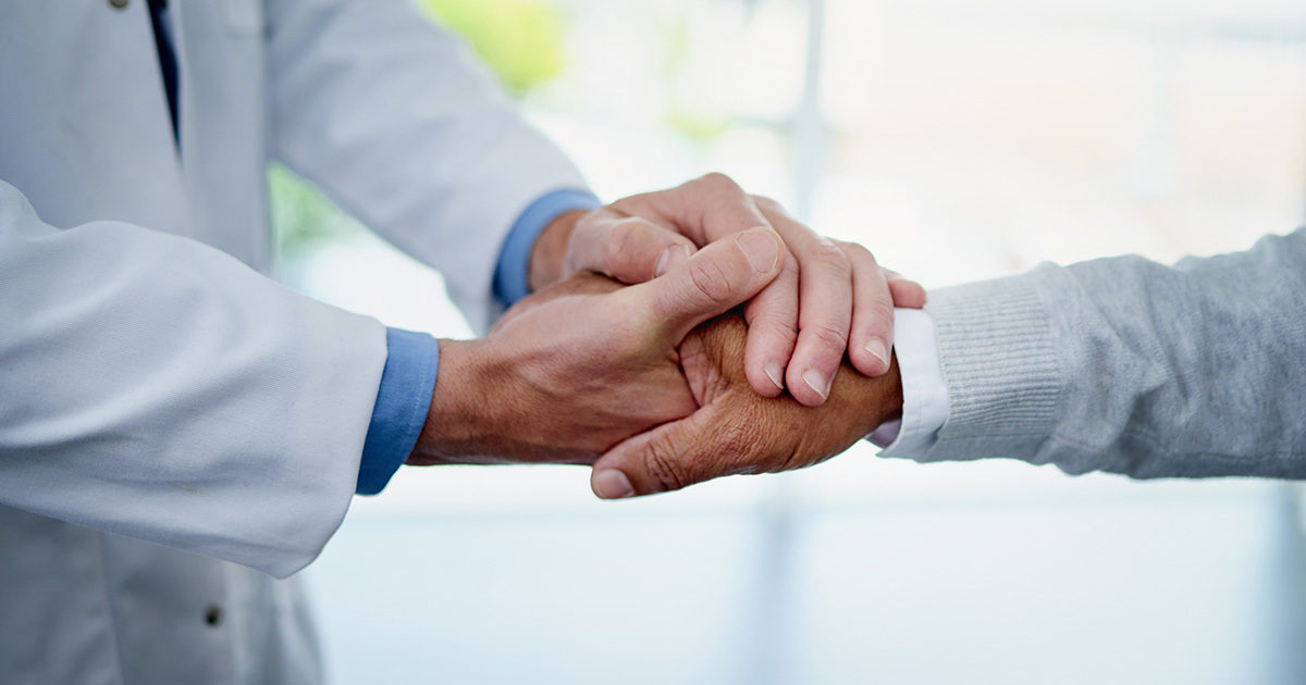 Close-up of a doctor in a white coat supportively holding a patient's hand.