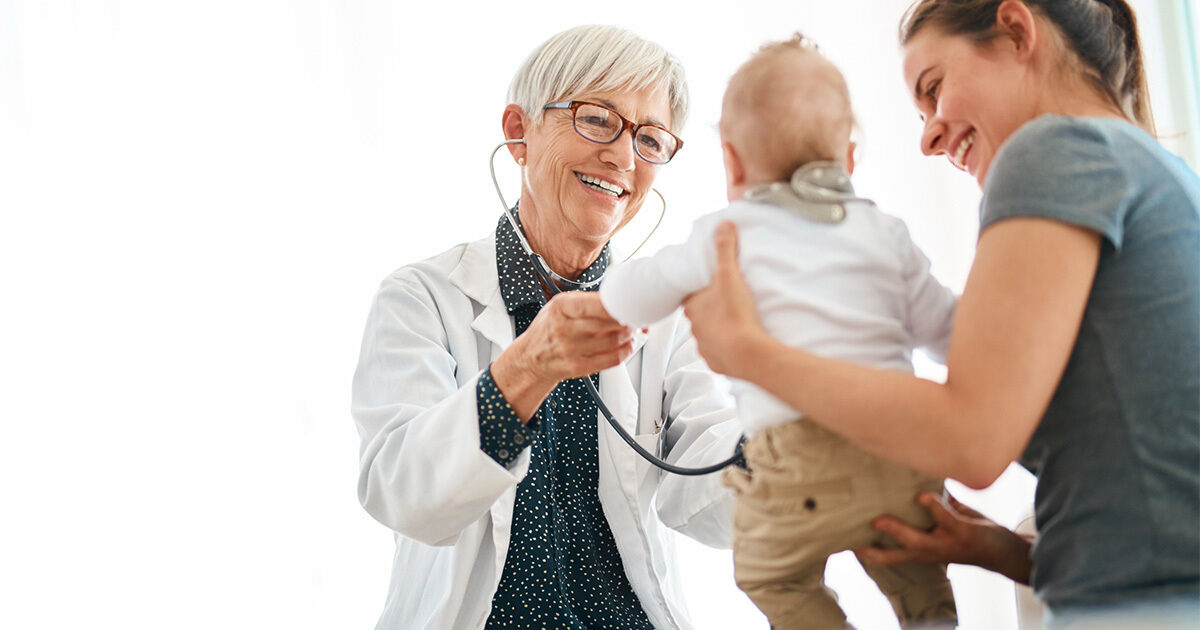 A mother holds her baby up to a smiling doctor holding a stethoscope.