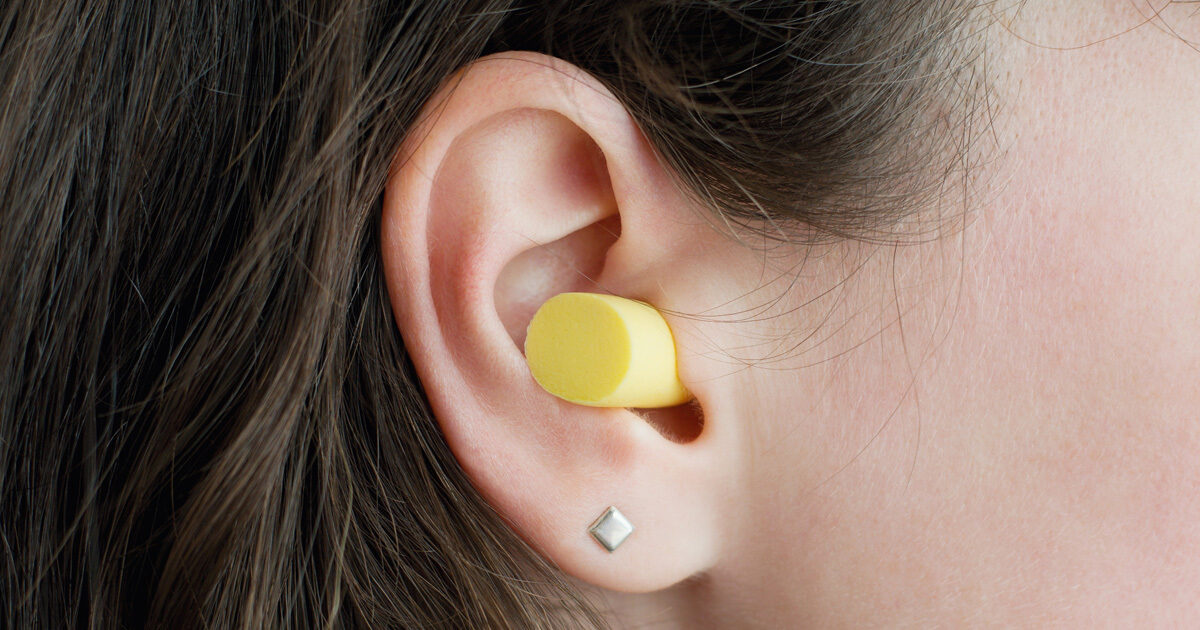 A closeup of a woman's ear is shown with silver studs and a yellow earplug.