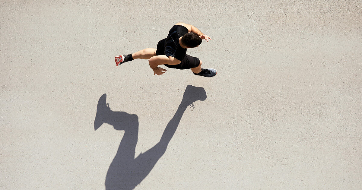 A man running as seen from above, casting a long shadow on the ground.