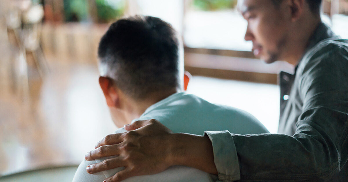 A young man places his arm around the shoulders of a loved one.