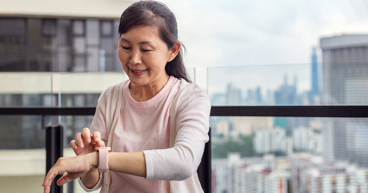 A woman in a pink shirt smiles and touches her smartwatch.