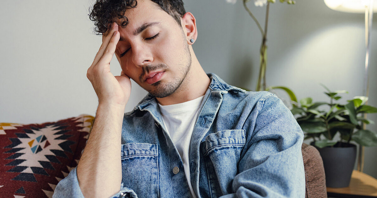 A man in a denim jacket closes his eyes and rests his head in one hand.