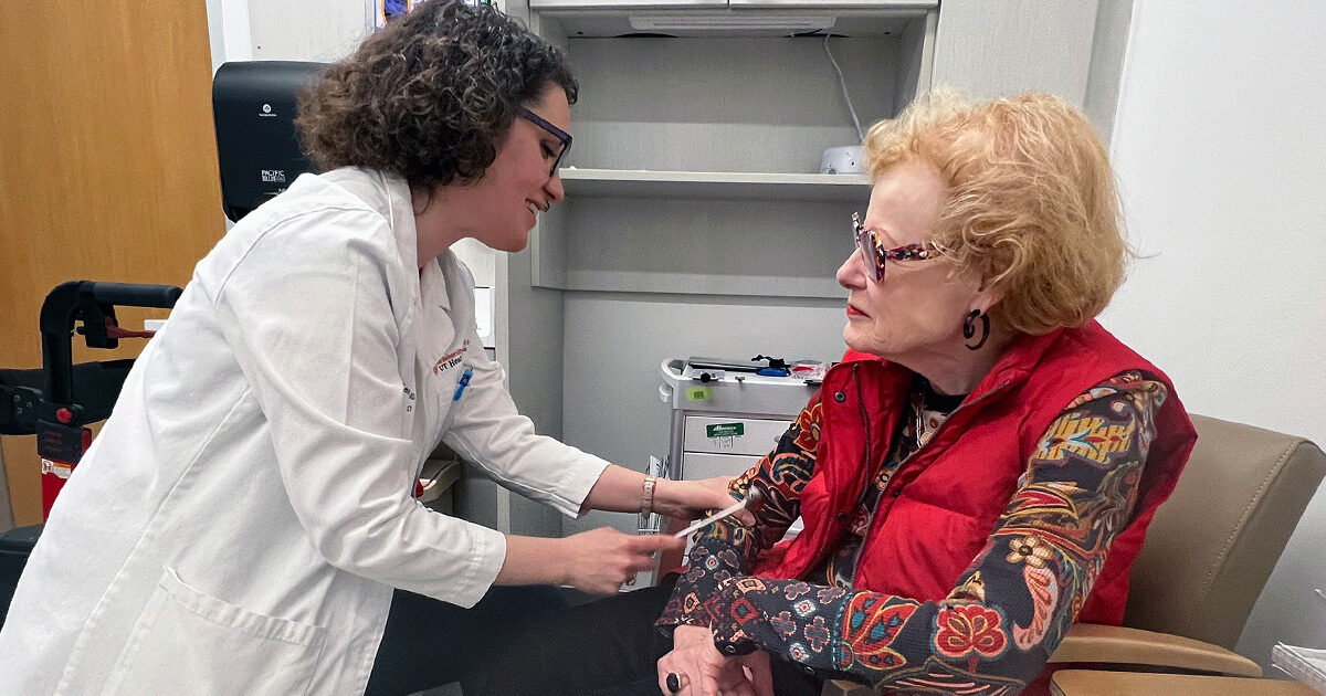 Leoráh Freeman, MD, PhD, performing a reflex test on Vicki Almond in an exam room.