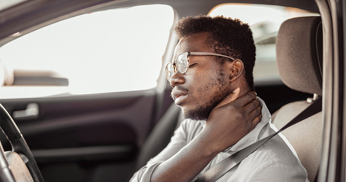 Man cradling his neck in pain in the front seat of his car.