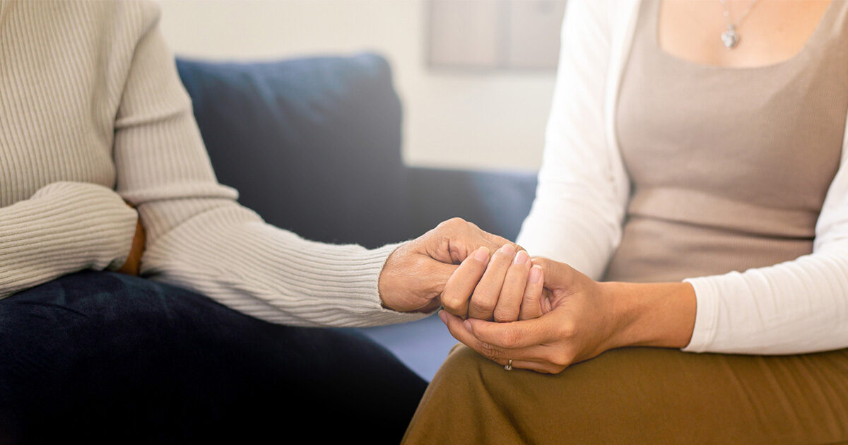 A closeup of two middle aged women holding hands in a supportive way