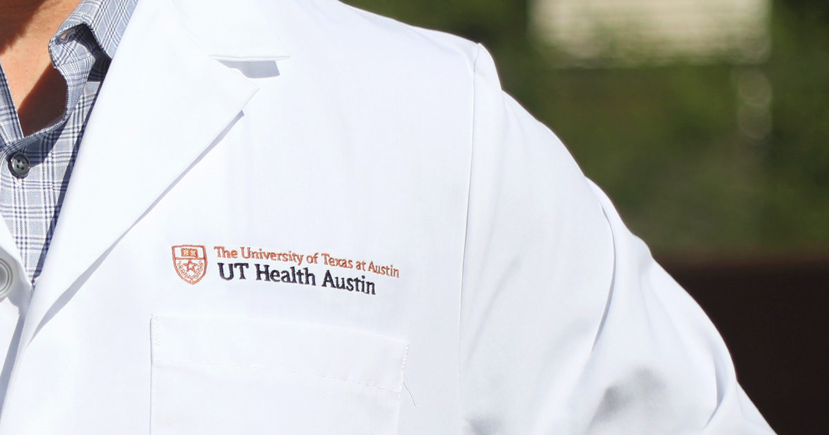 A close-up of a physician's coat left shoulder and chest showing the UT Health Austin logo.