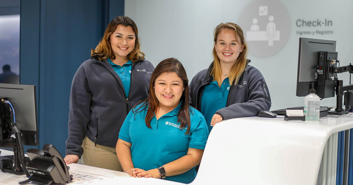 Three female members of the UT Health Austin concierge team smile at the camera.