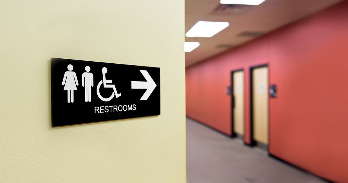 A bathroom sign with an arrow pointing down a long hallway.