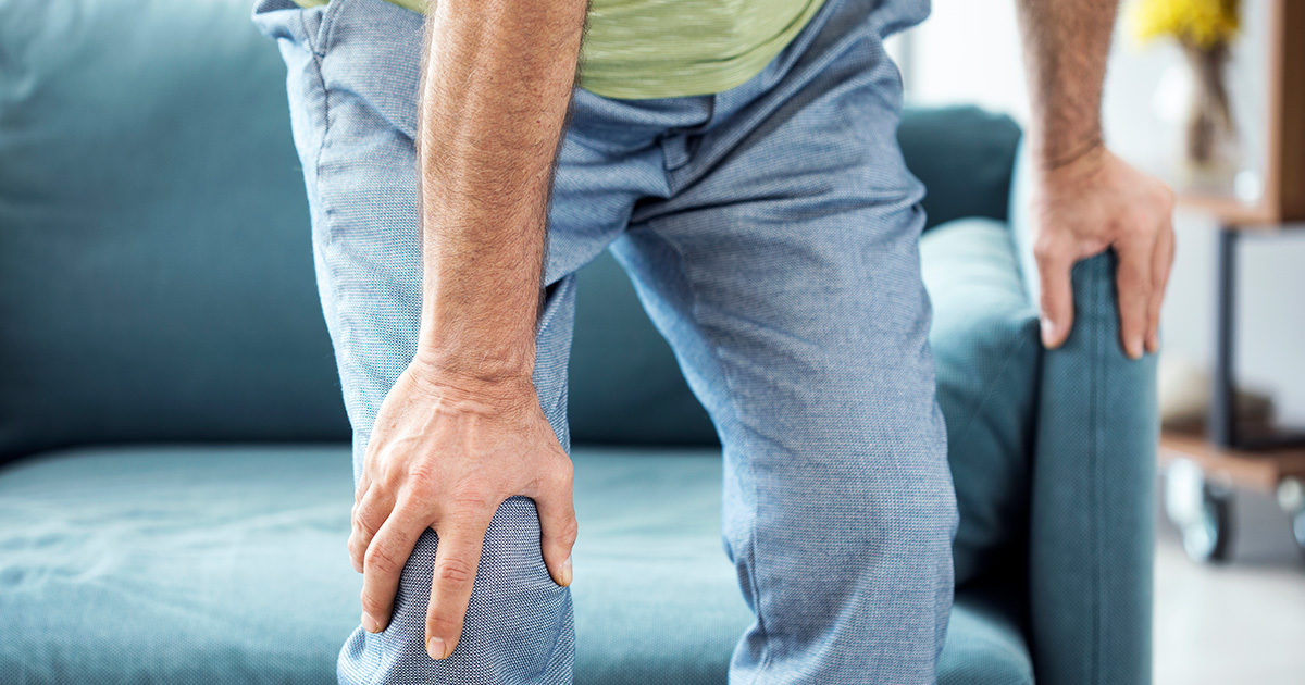 Closeup view of a man bent over in discomfort, clutching his knee.