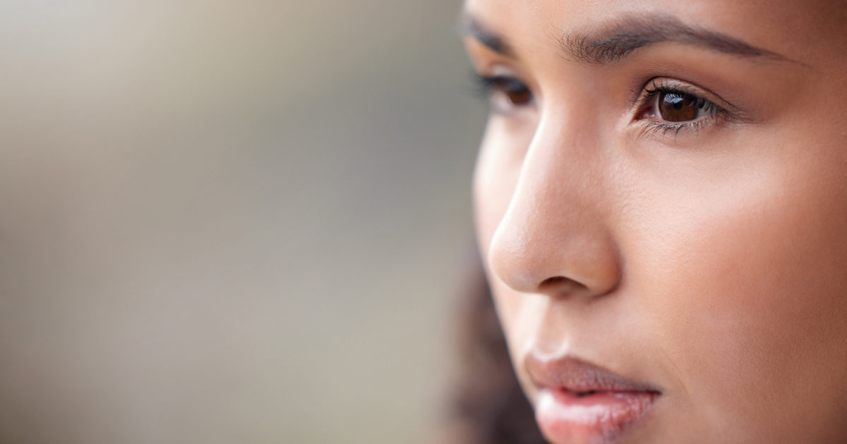 A young woman with brown eyes looks off in the distance with a blurry background behind her.