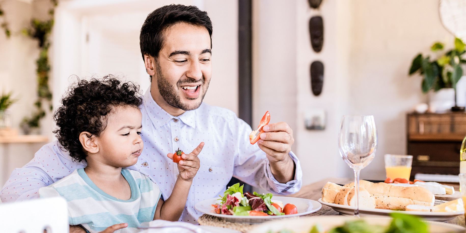 A man and his son sit at a table filled with food, sharing a salad.