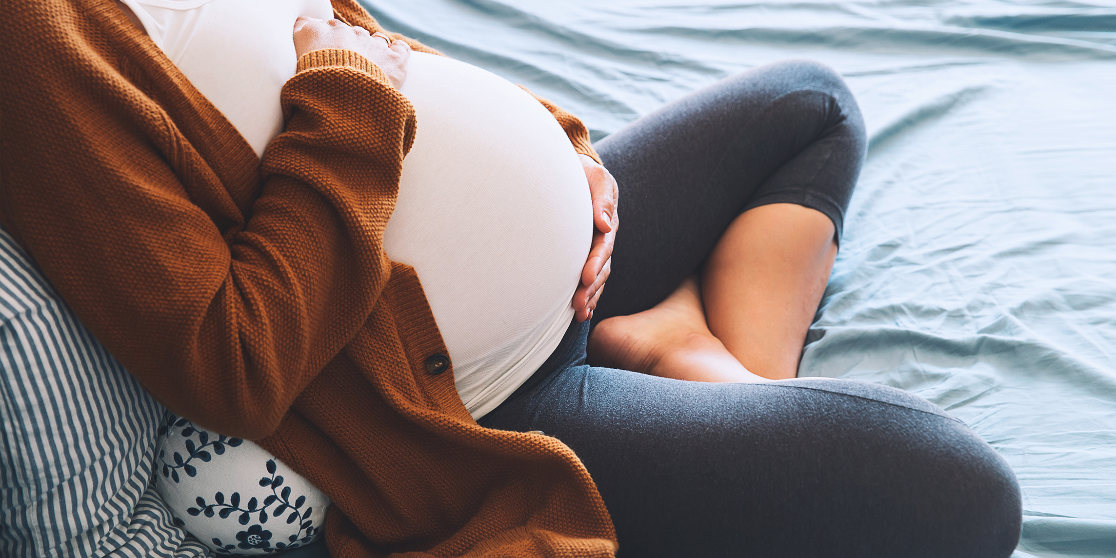 A pregnant woman with her head out of frame reclines on pillows.