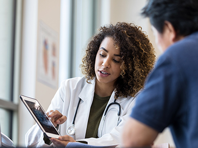 A Black female doctor shares a tablet image with a patient that she is consulting.