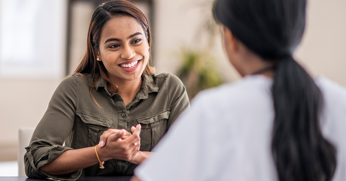 A young woman smiles at another woman with her back to the camera.