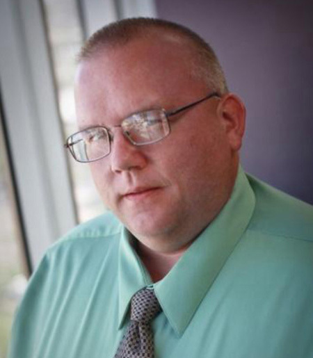 A headshot of Tim Martin wearing a green shirt and necktie.