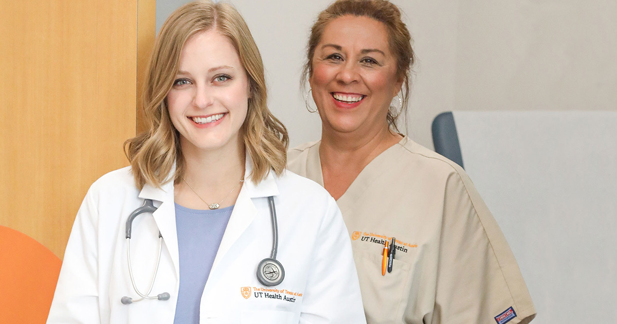 Walk-in Clinic health care providers, nurse practitioner Emmy and MA Brenda, stand together in an exam room smiling at the camera.