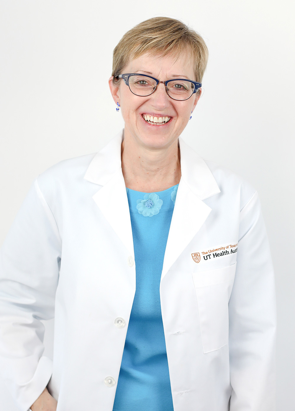 Joie Flees wearing a white coat and smiling in front of a white backdrop.