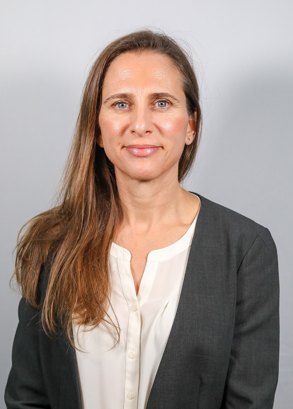 Pediatric psychologist Alexandra Lamari-Fisher, PhD, wearing a gray jacket and white blouse and smiling in front of a white backdrop.