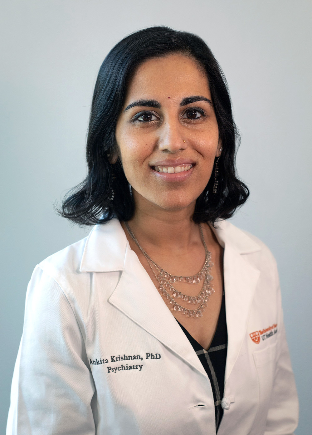Pediatric psychologist Ankita Krishnan, PhD, wearing a white coat and smiling in front of a white backdrop.