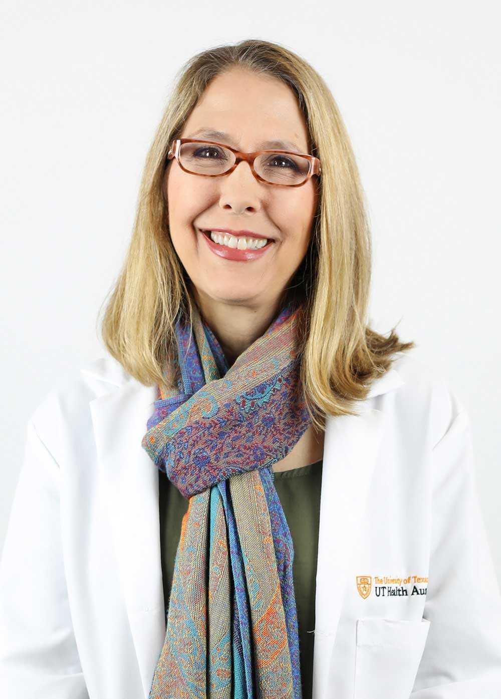 Audrey Baum wearing a white coat and smiling in front of a white background.