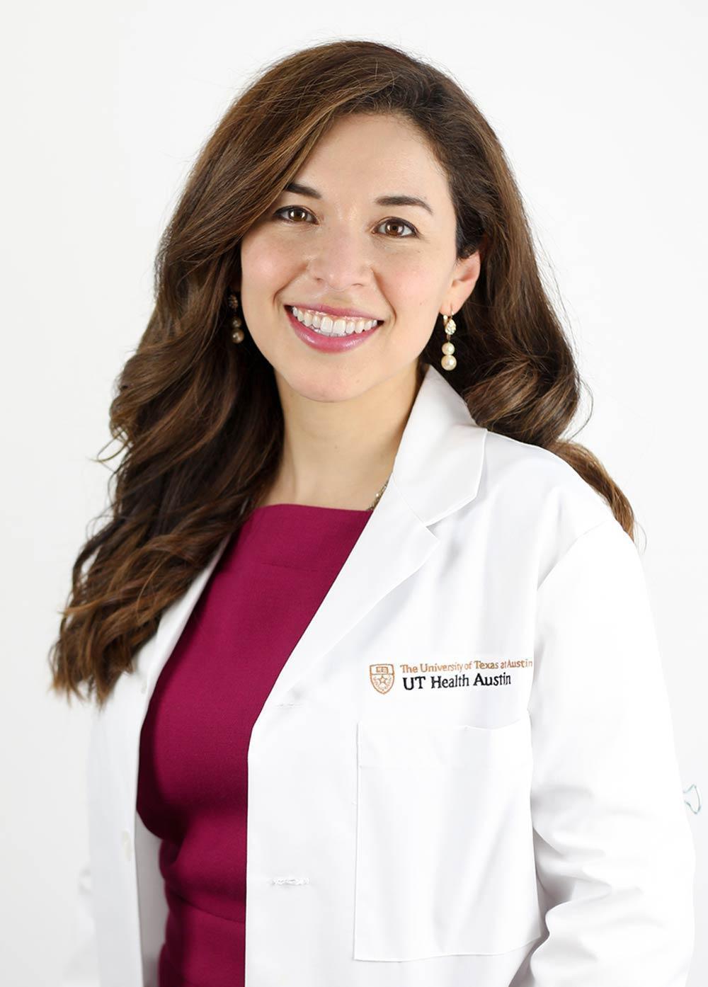 Dr. Christina Salazar wearing a white coat and smiling in front of a white backdrop.