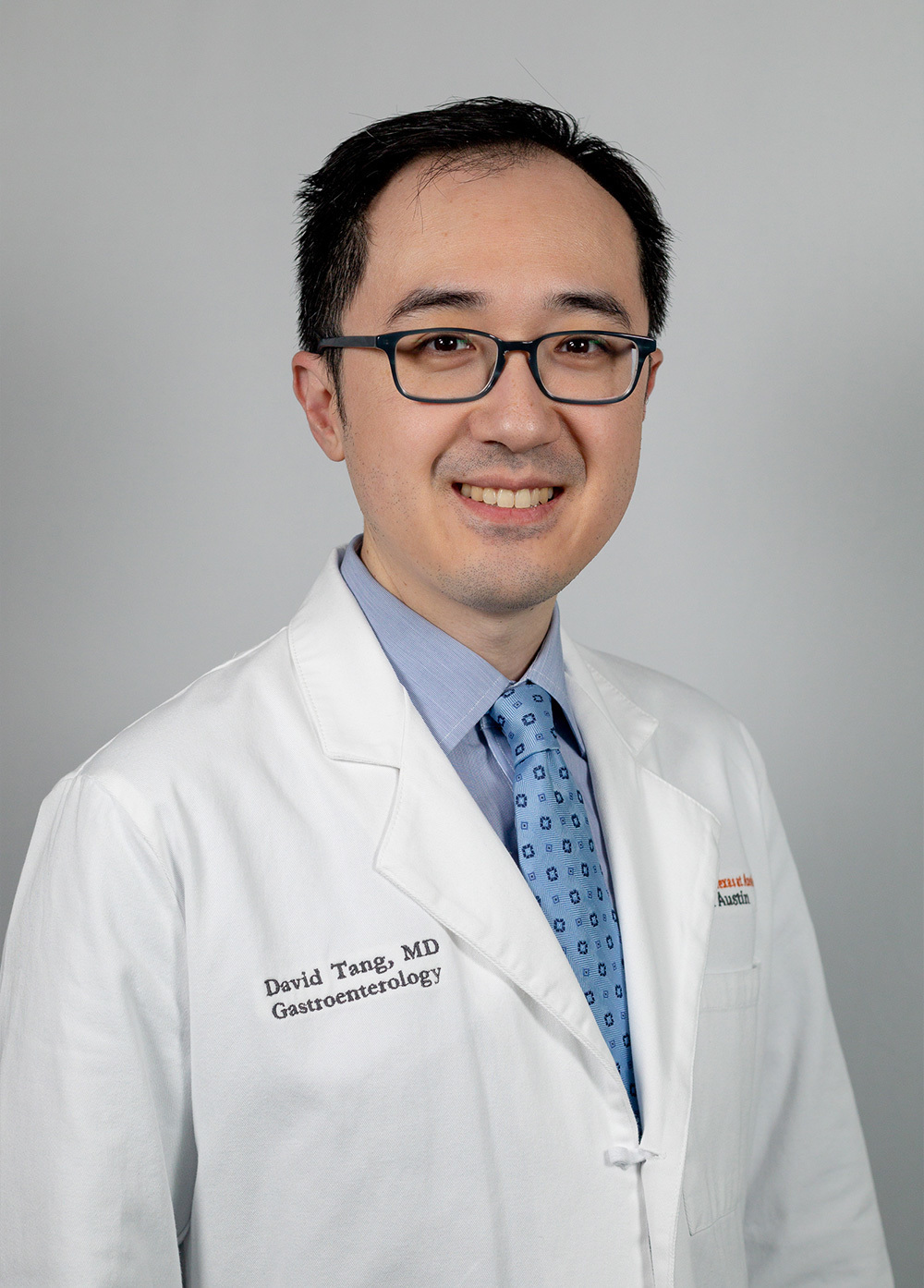 Gastroenterologist David Tang, MD, wearing a white coat and smiling in front of a white background.