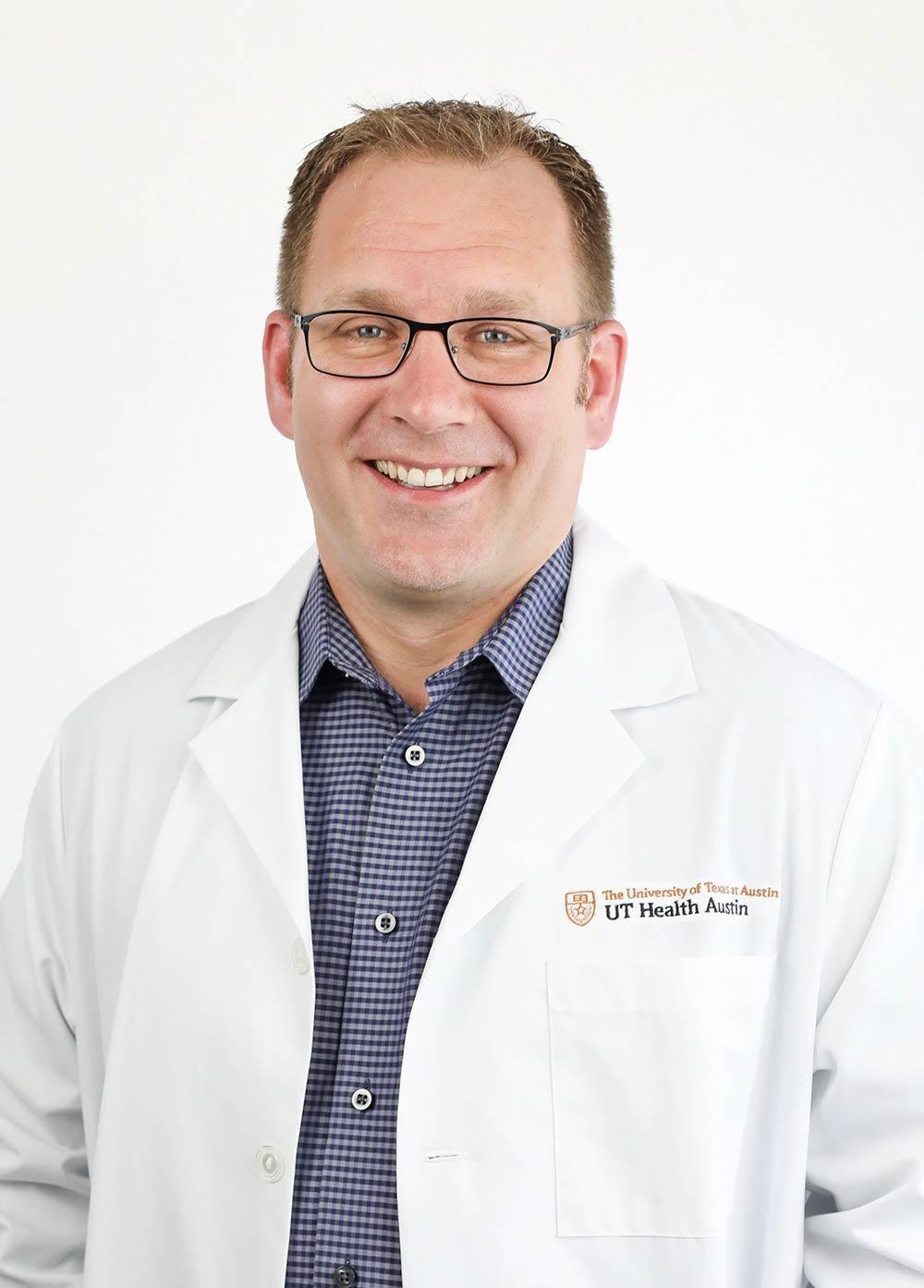 Devin Williams wearing a white coat and smiling in front of a white backdrop.