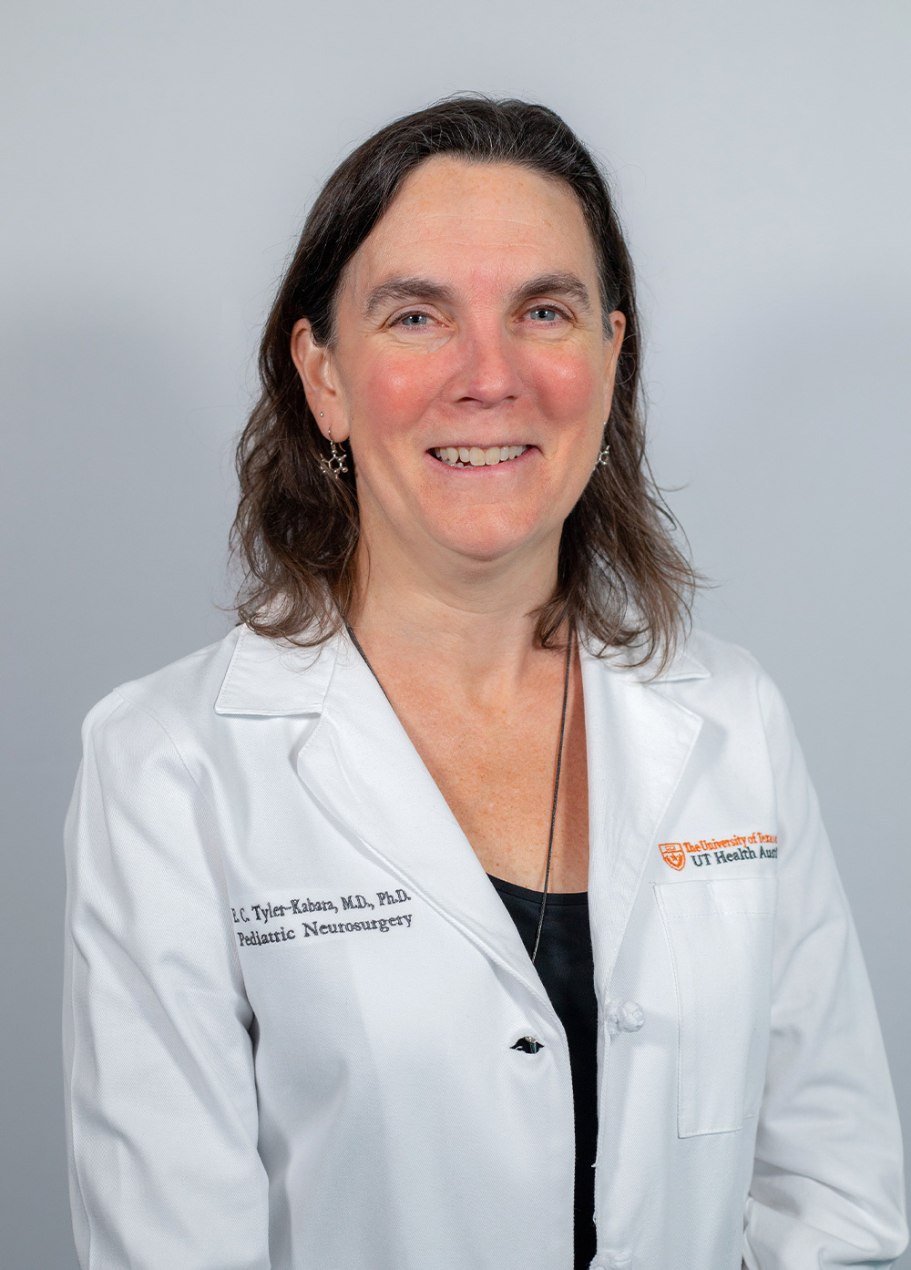 Pediatric neurosurgeon Elizabeth C. Tyler-Kabara, MD, PhD, smiling and wearing a white coat in front of a white backdrop.