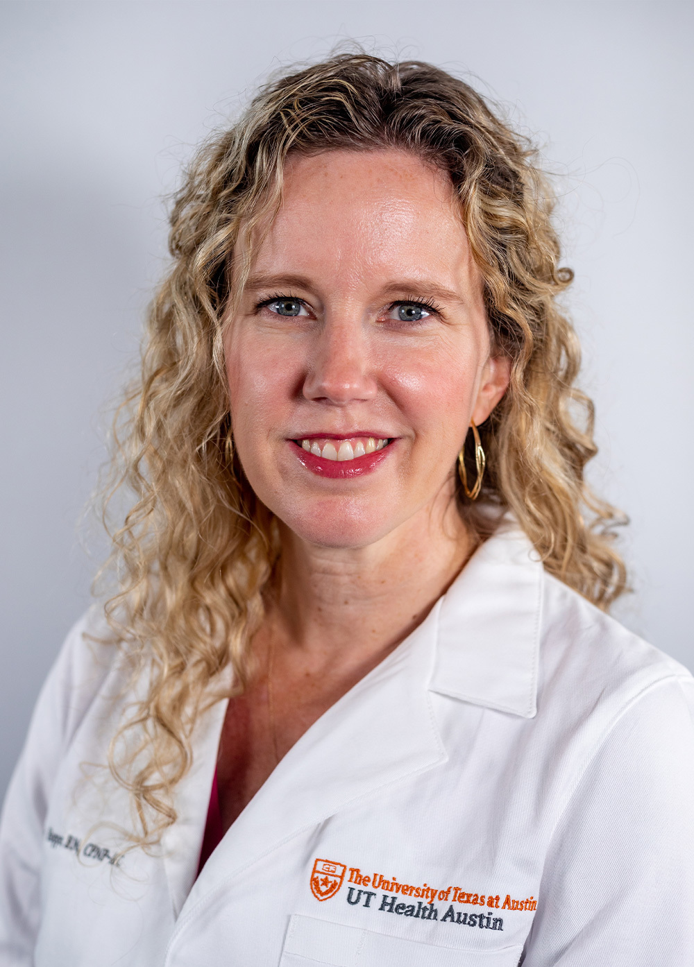 Pediatric nurse practitioner Emily Hopper, MSN, APRN, CPNP-AC, wearing a white coat and smiling in front of a white backdrop.