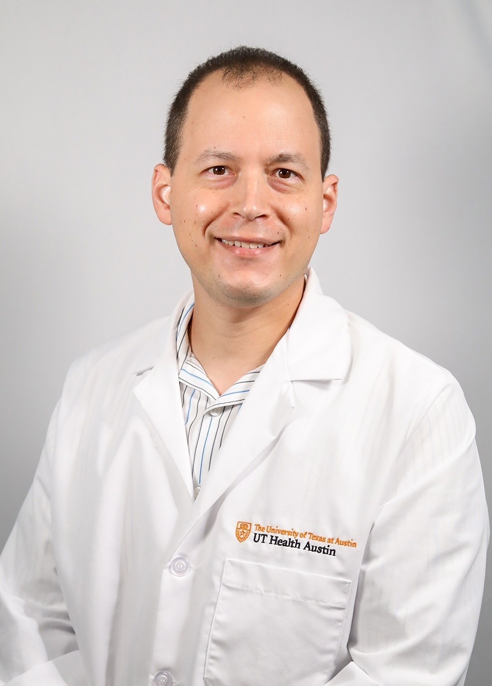 Dr. Gabriel Garza wearing a white coat and smiling in front of a white backdrop.