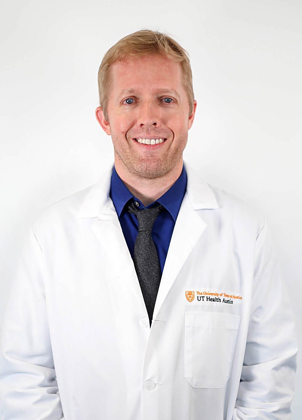 Dr. John Bertelson wearing a white coat and smiling in front of a white backdrop.