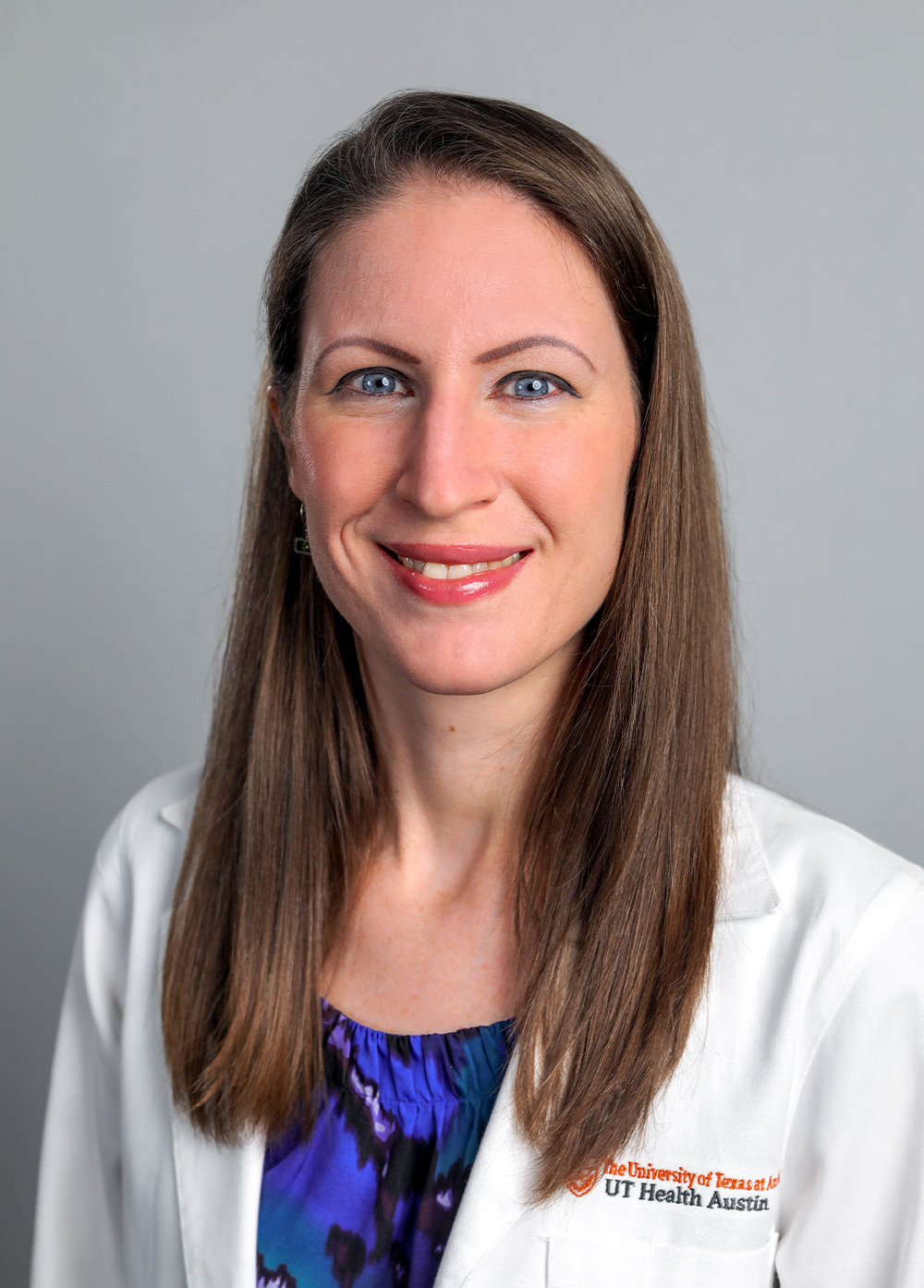 Pediatric cardiac critical care intensivist Katie Colman, MD, wearing a white coat and smiling in front of a light gray backdrop.