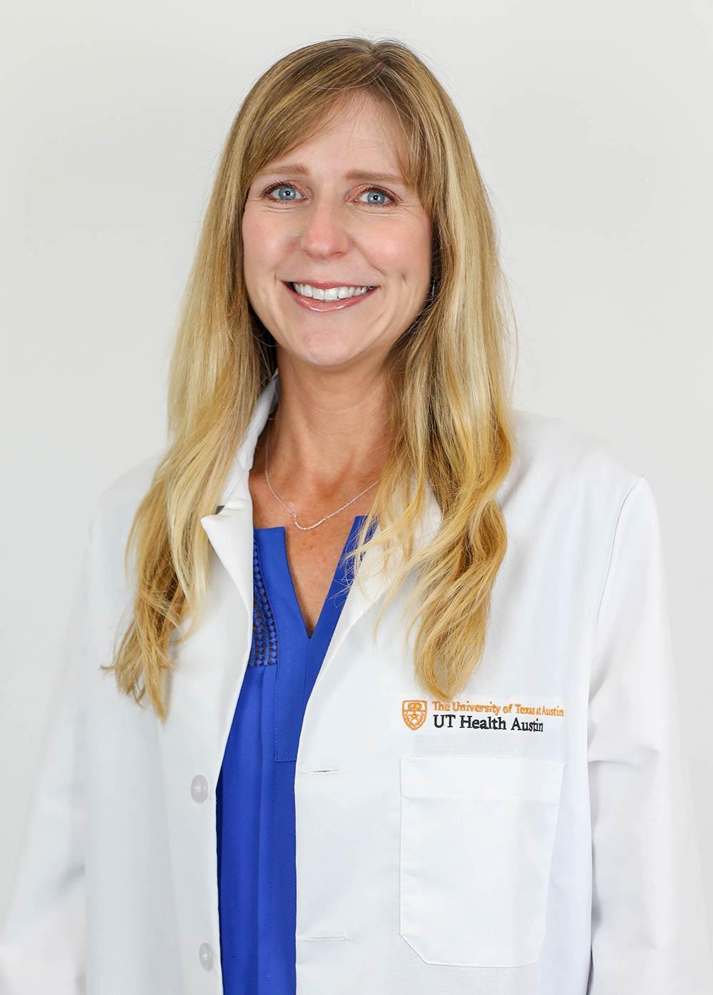 Kristin Vinueza wearing a white coat and smiling in front of a white backdrop.