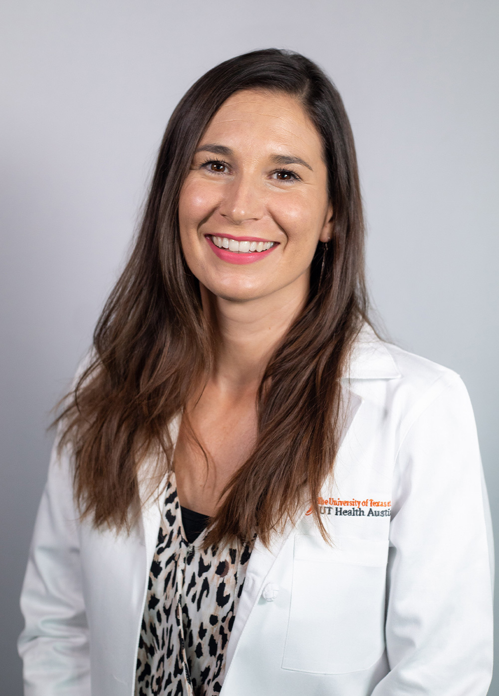 Lindsay Kozicz wearing a white coat and smiling in front of a white backdrop.