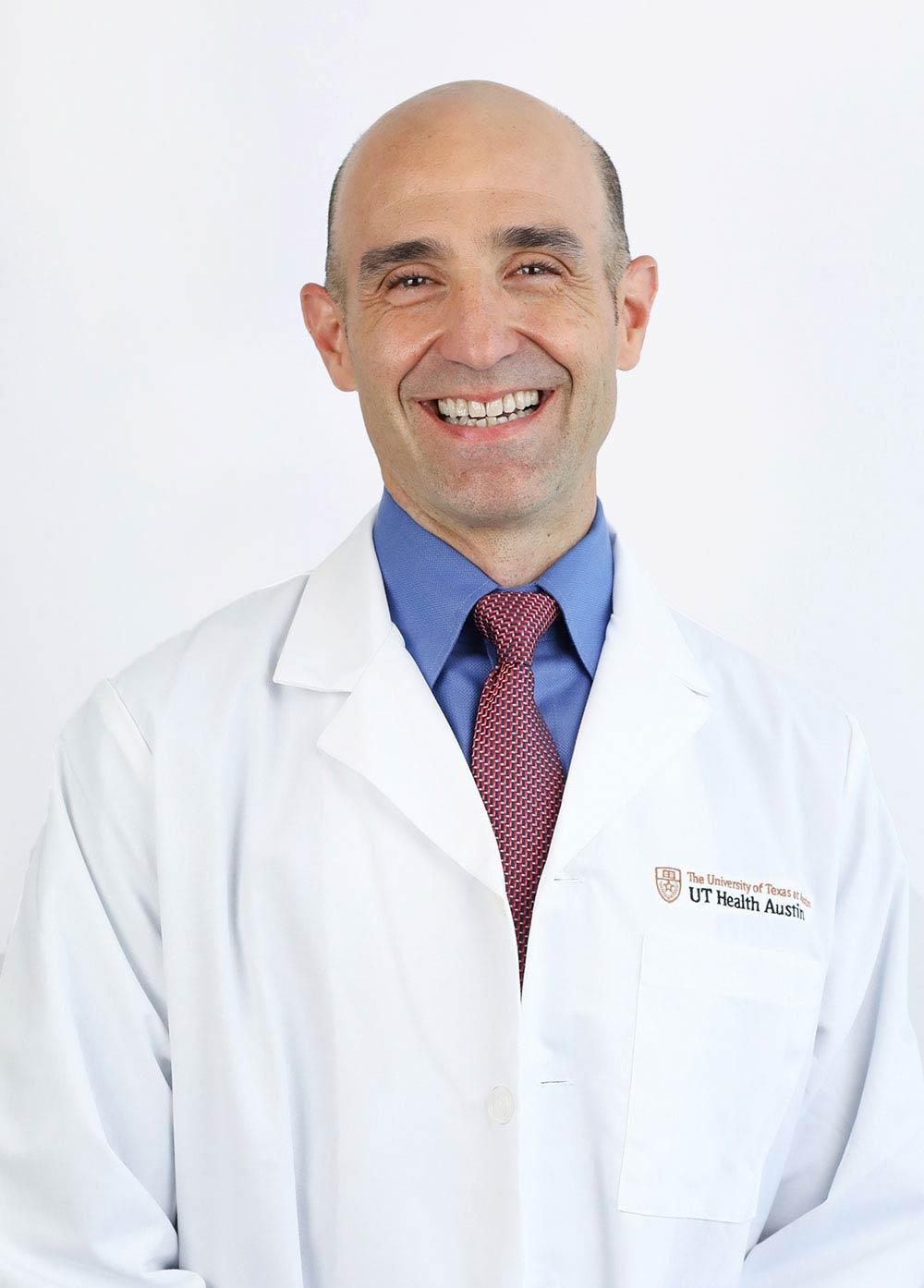 Dr. Mark Queralt wearing a white coat and smiling in front of a white backdrop.