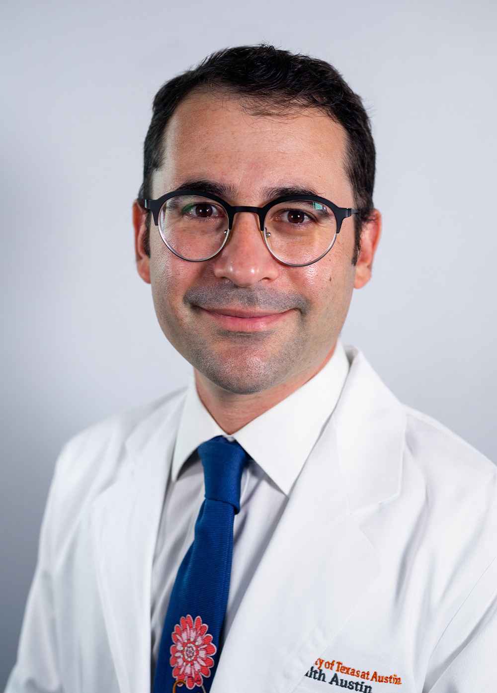 Obstetrician-gynecologist Max Holtz, MPH, wearing a white coat and smiling in front of a white backdrop.