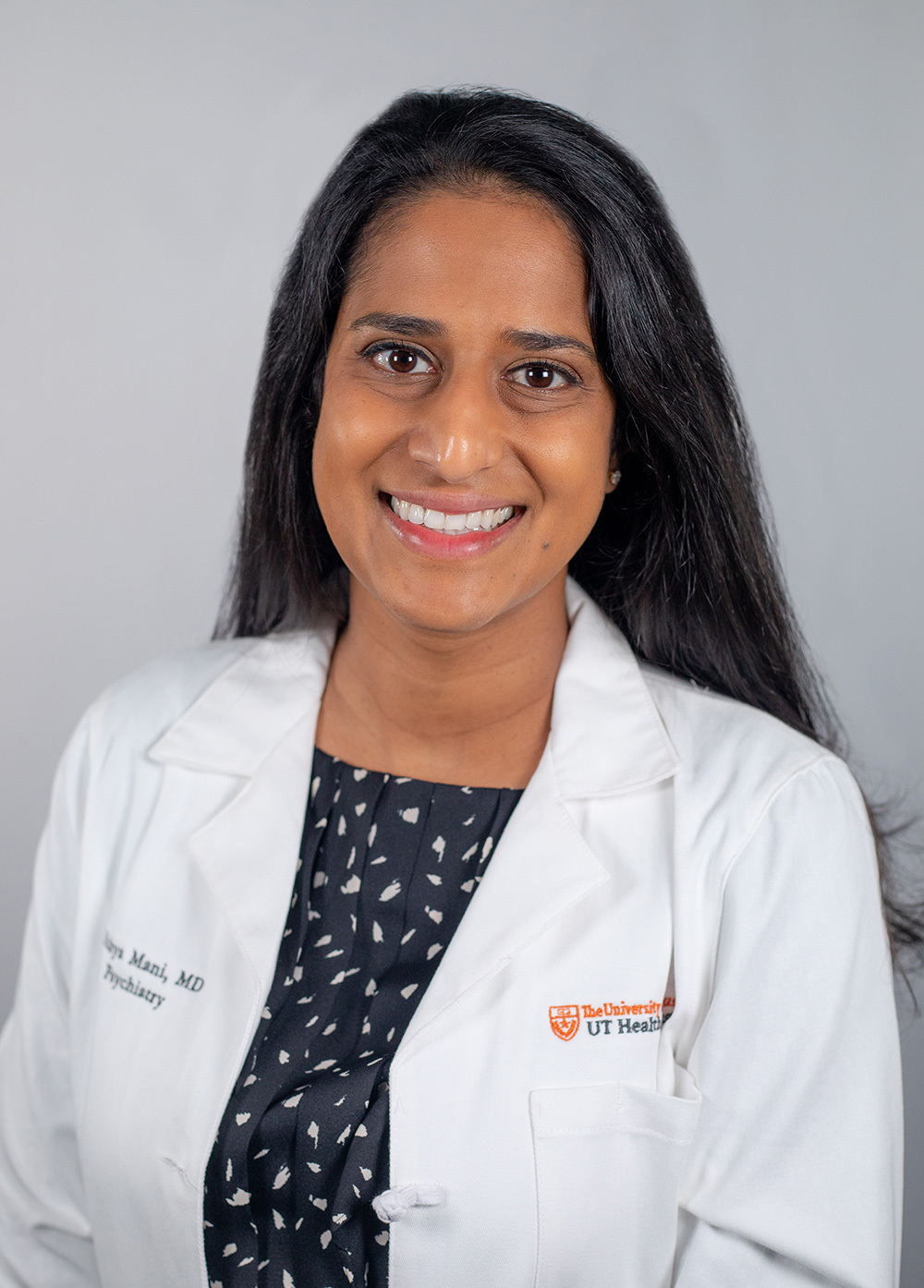 Child and adolescent psychiatrist Nithya Mani, MD, wearing a white coat and smiling in front of a white backdrop.